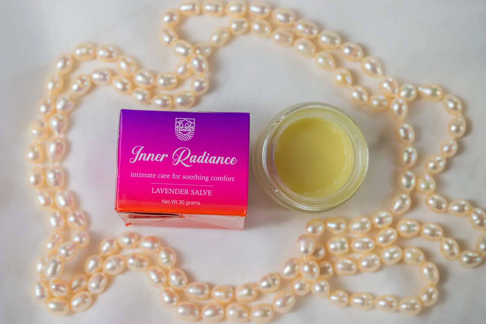 A jar of creme sits next to pearls.